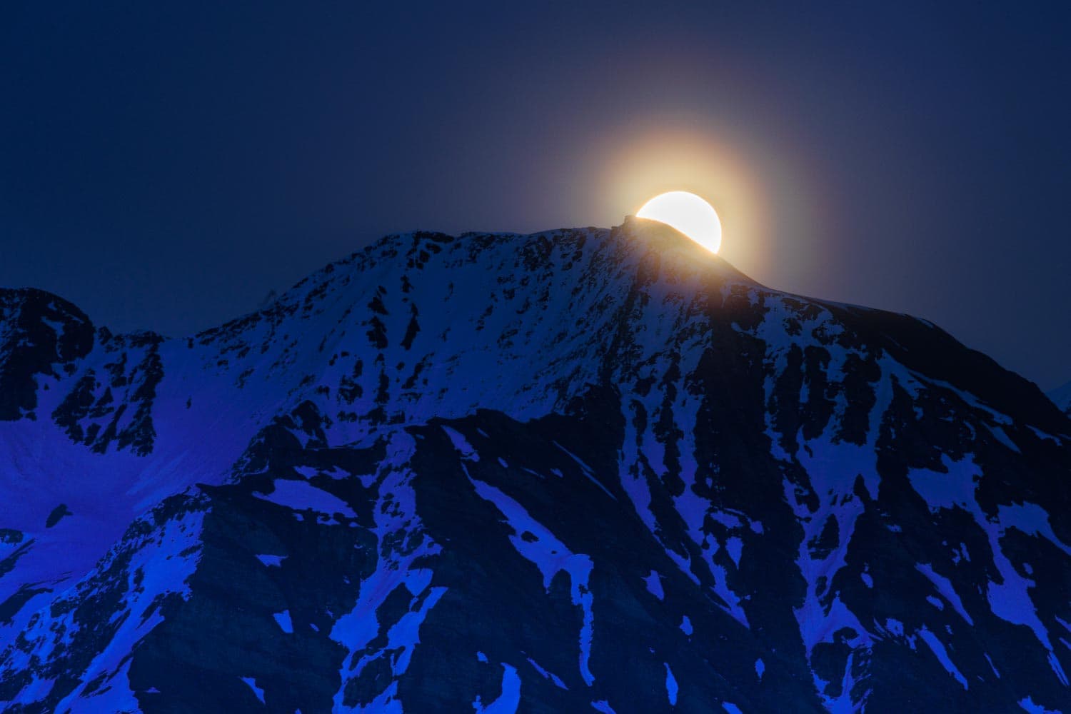 Vollmond-Aufgang (Flower Moon) hinter einem verschneiten Bergspitz